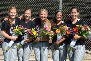 softball players smiling in a group, holding flowers for their senior celebration