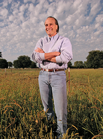 Dan Guistina with arms crossed and smiling in a green field at the University Farm