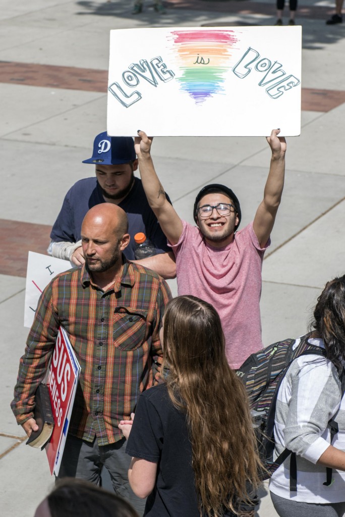 Seve Christian (right) holds up a sign that reads "Love is Love" as students speak back against persecution on campus from one man who only wanted to be identified as Ron (left), expressing the difference of opinions about religious views about Jesus Awareness Day on Wednesday, April 13, 2016 in Chico, Calif. (Jason Halley/University Photographer)