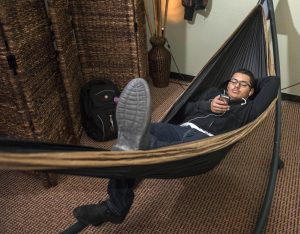 Young man laying in a hammock, relaxed and reading from his mobile phone.