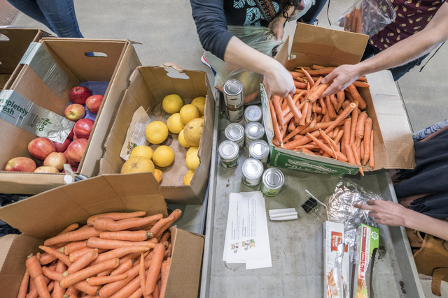 Several hands reach into boxes of carrots and apples to put them into bags during CalFresh Day.