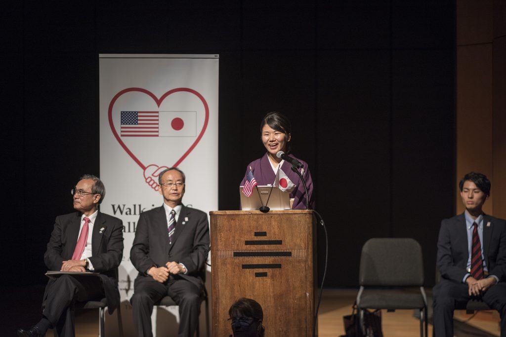 Soushin Ikeda, dressed in a kimono, addresses the audience from a podium