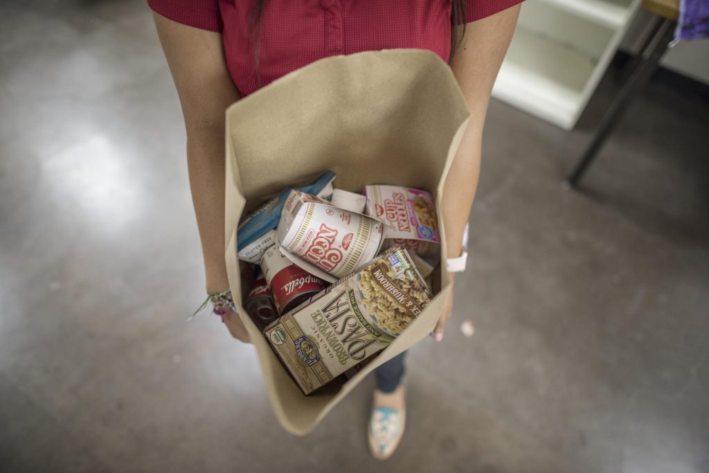 Shot looking down into a grocery bag held by a student, filled with pantry items such as pasta and noodles.