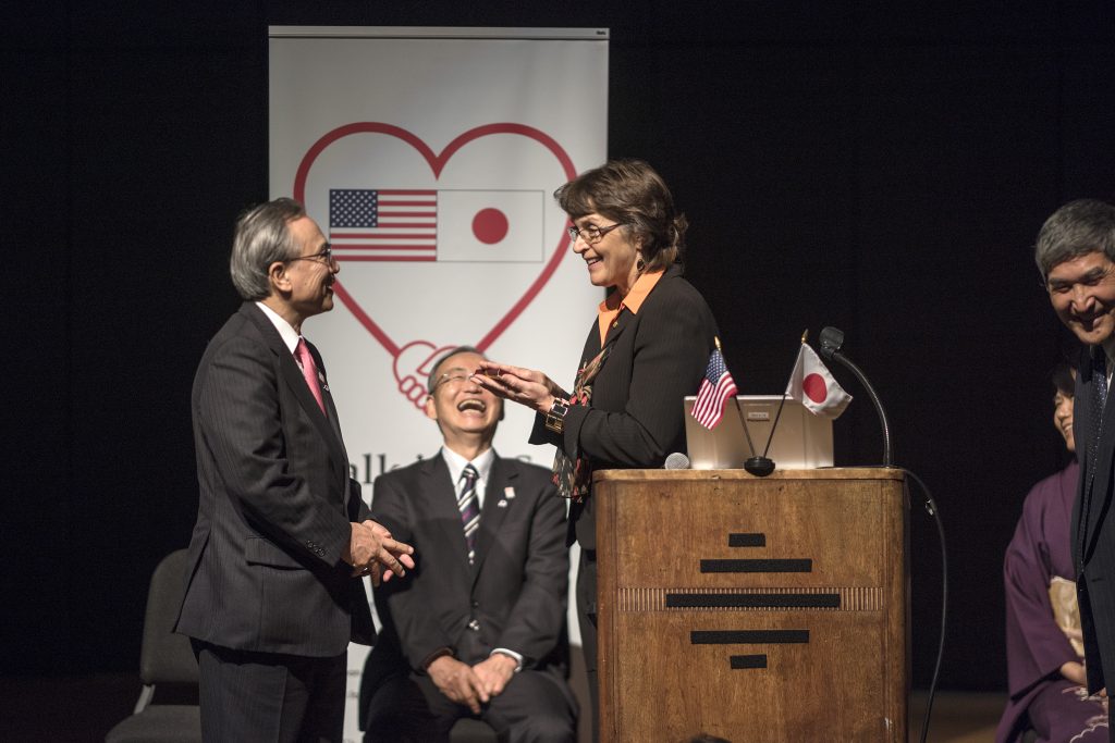 President Hutchinson presents a small gift to Ambassador Oshima on stage.