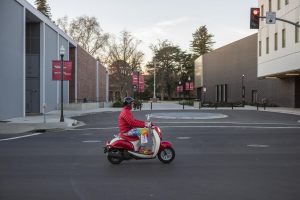 Joe Crotts rides his scooter in front of the circle driveway at Second Street in front of the Chico State campus.