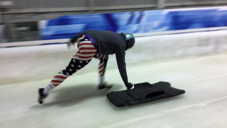 Brooke pushing a skeleton sled down the icy course in Team USA clothing