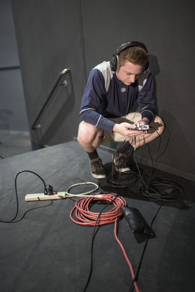 Kyle Bailey crouches over cords to set up audio equipment