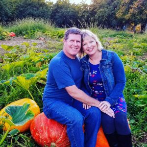 Mike and Corina Yetter sitting on pumpkins in a field, smiling.