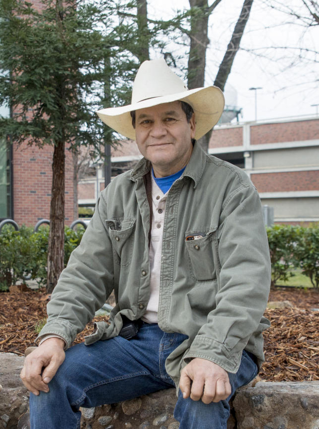 Ricardo Carrillo sits on a stone wall he constructed wearing a white cowboy hat.