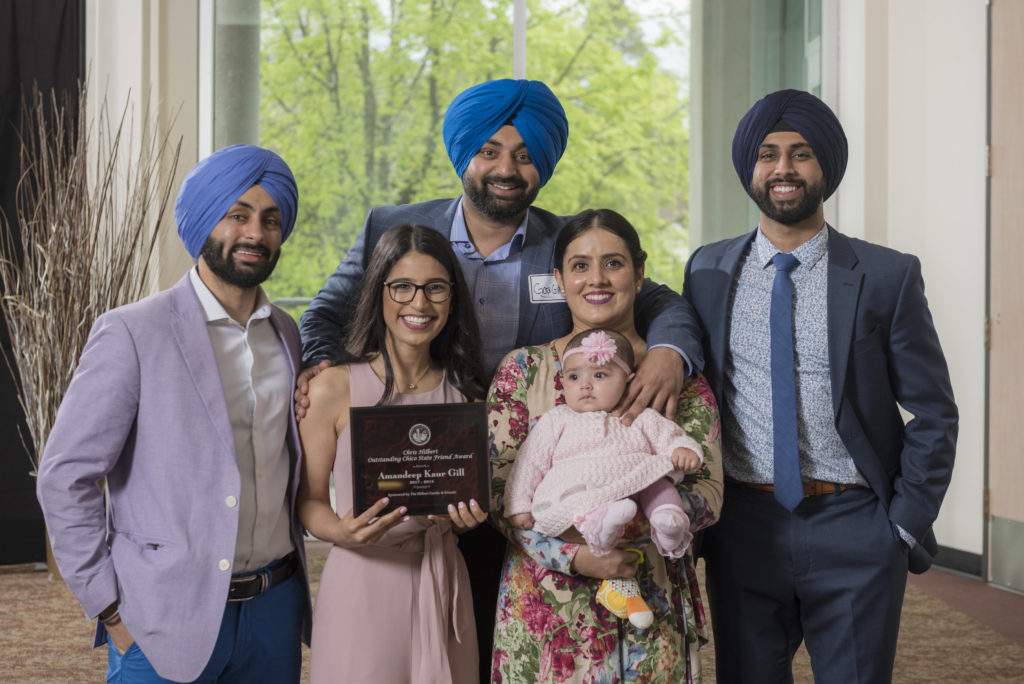 Amandeep Kaur Gill holds a plaque honoring her Outstanding Friend award, standing among her two brothers, mother, father, and baby niece.