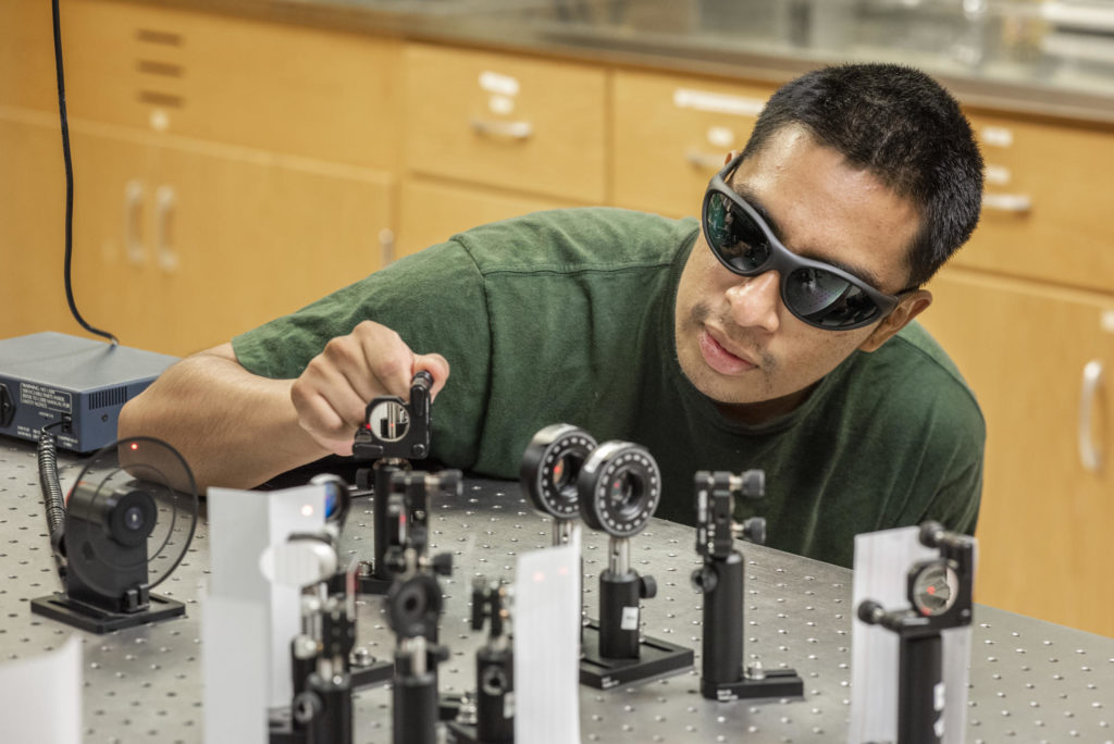 Eddie Cruz, wearing protective glasses, adjusts laser instruments on a tabletop.