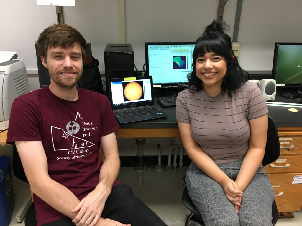 Two students pose for a photo near research computers.