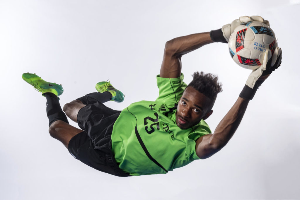 Damion Lewis jumps through the air to catch a soccer ball in a photo studio.
