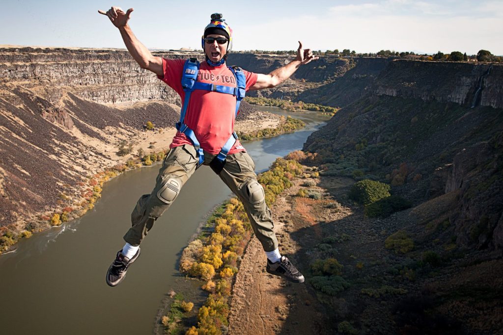 Miles Daisher falls through the air, gesturing to the camera, as he BASE jumps over a river off the 486-foot-high I.B. Perrine Bridge in Twin Falls, Idaho.
