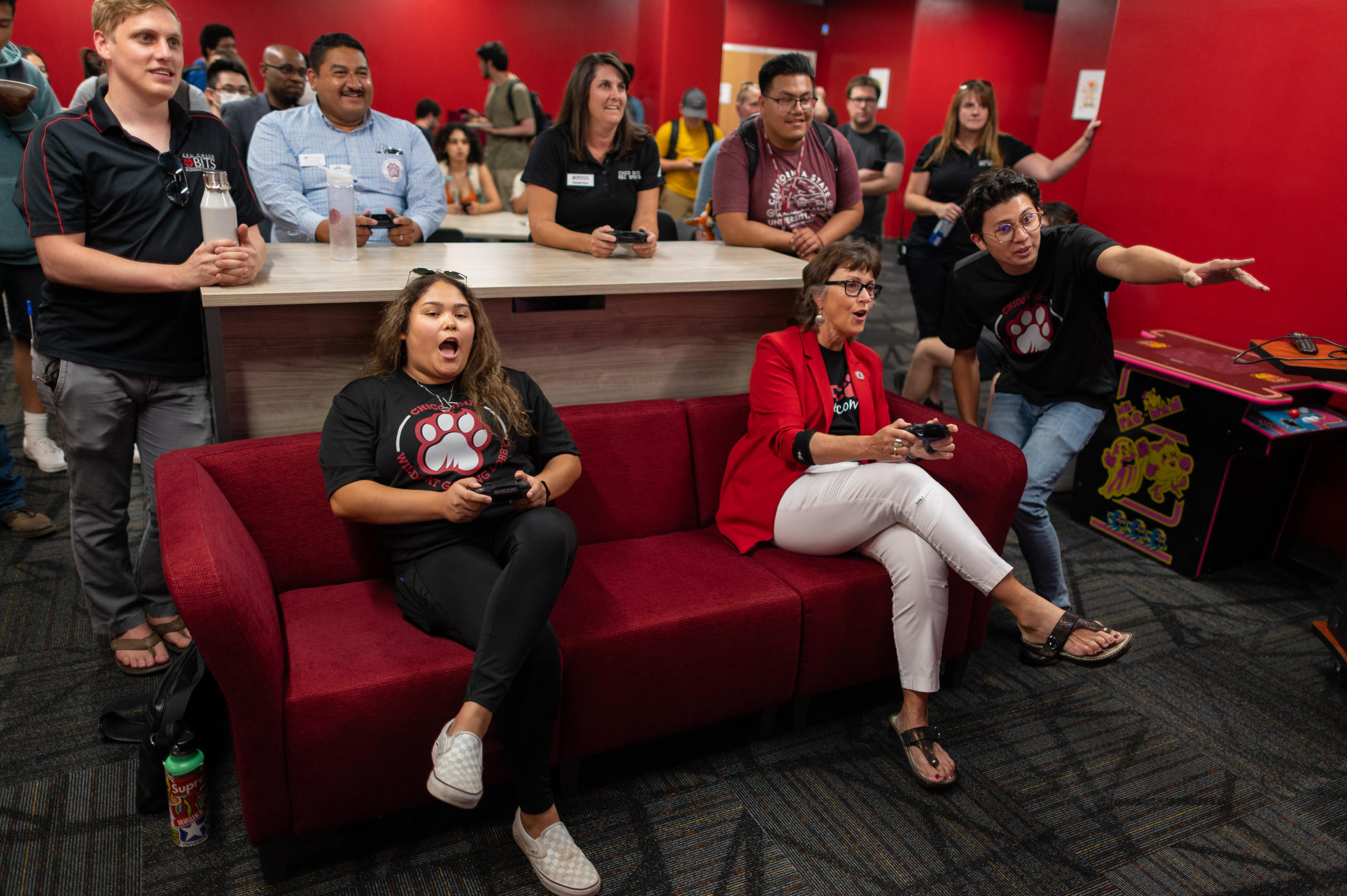 President Hutchinson and AS President Krystal Alvarez make extreme expressions as they play video games in the new gaming lobby while a crowd cheers them on from behind.