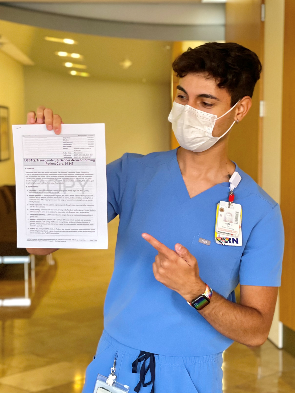 Un joven enfermero que usa batas y una máscara sostiene y señala una hoja de política para el cuidado de la salud.