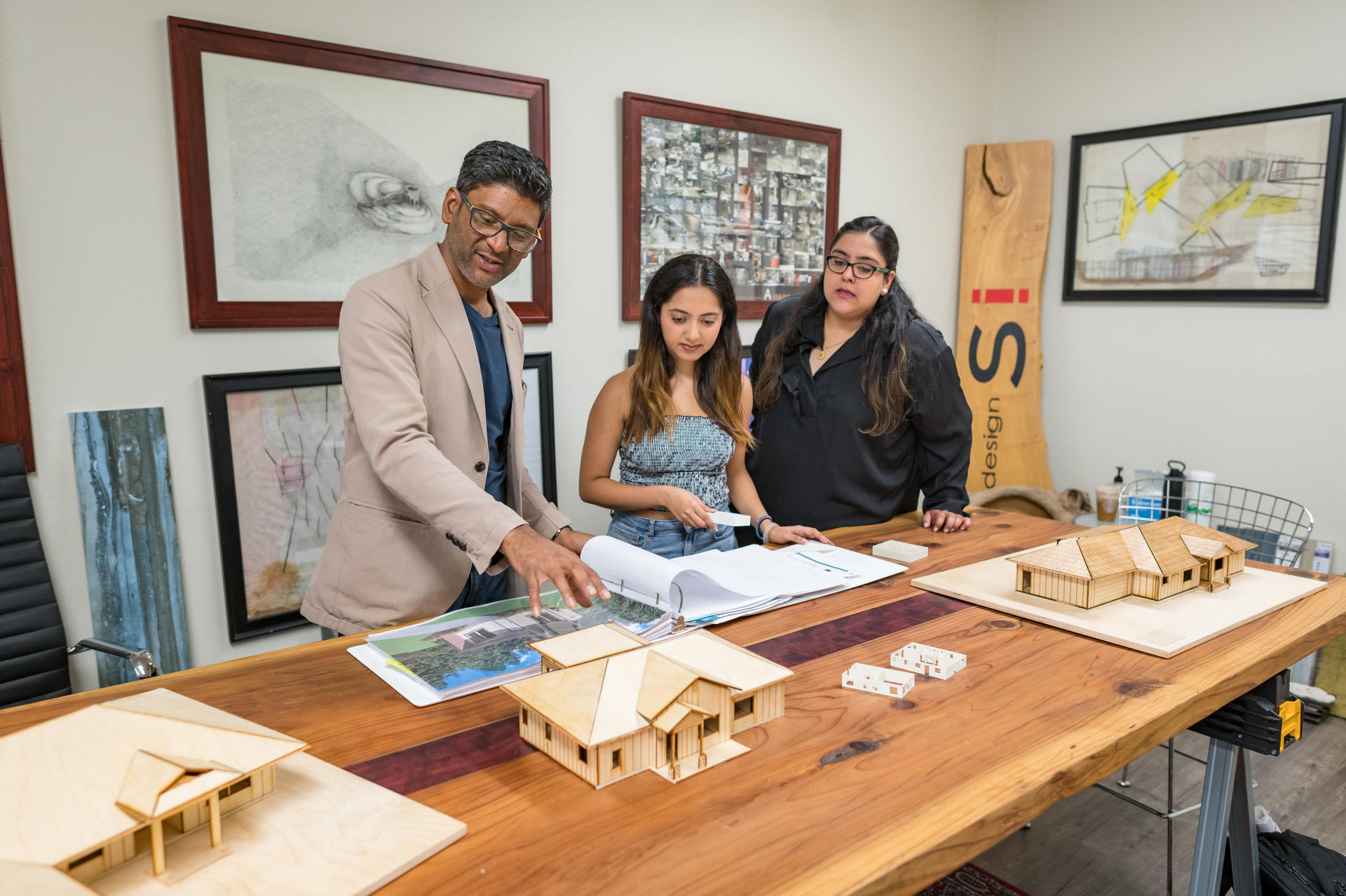 Rouben Mohiuddin, Charvi Grover, and Hira Namit discuss the floorplan designs with wooden models set on the table in front of them.