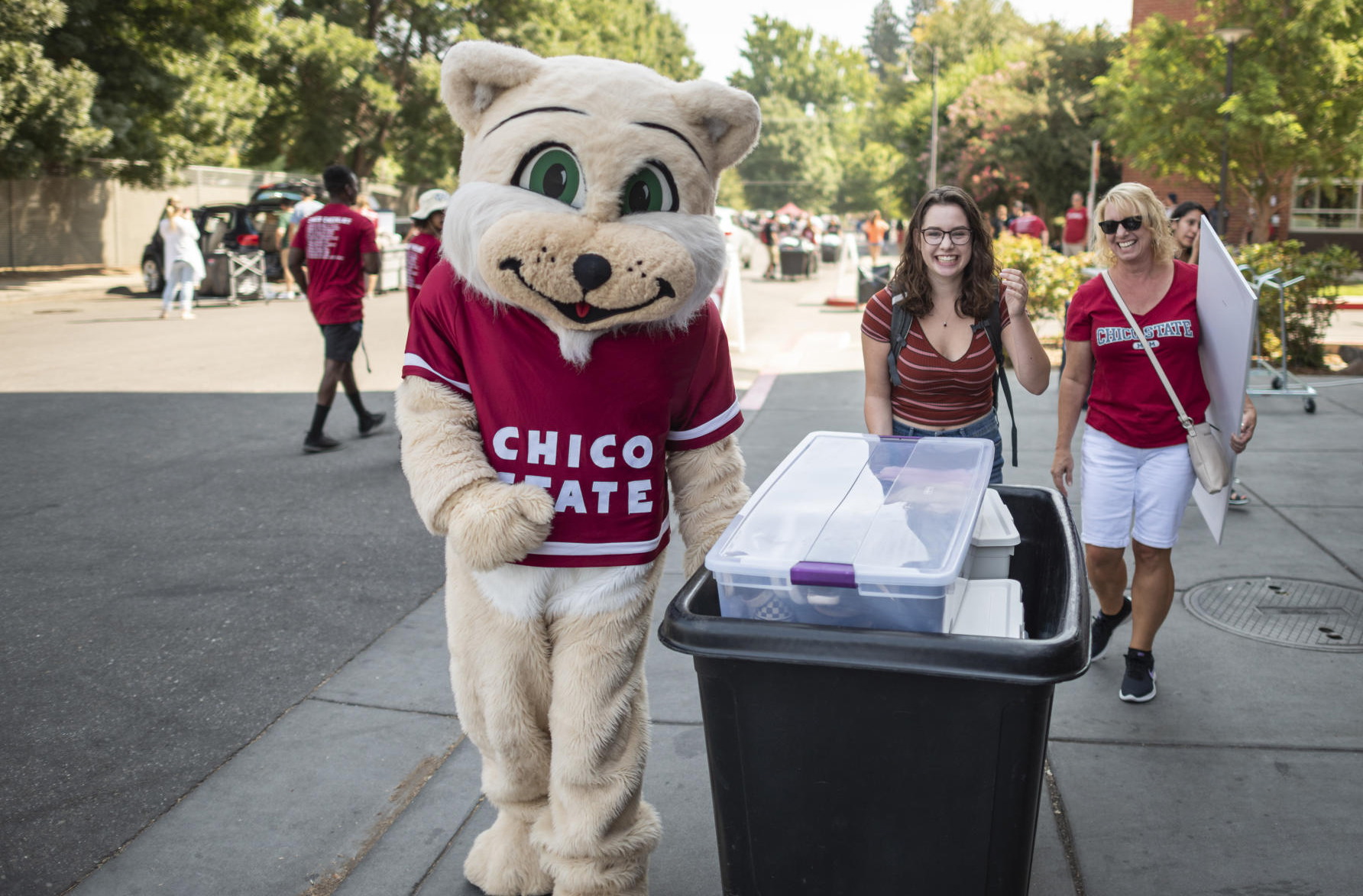 Willie the Wildcat helps a new student push a cart during move in