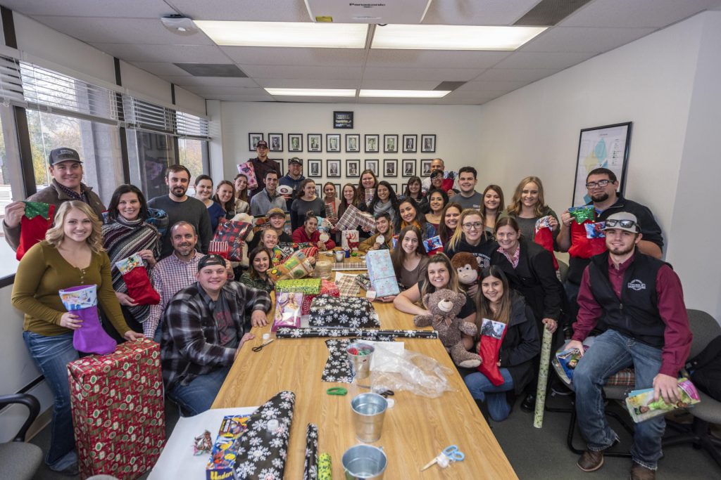The 32 students and other volunteers pose around a conference table covered in gifts.