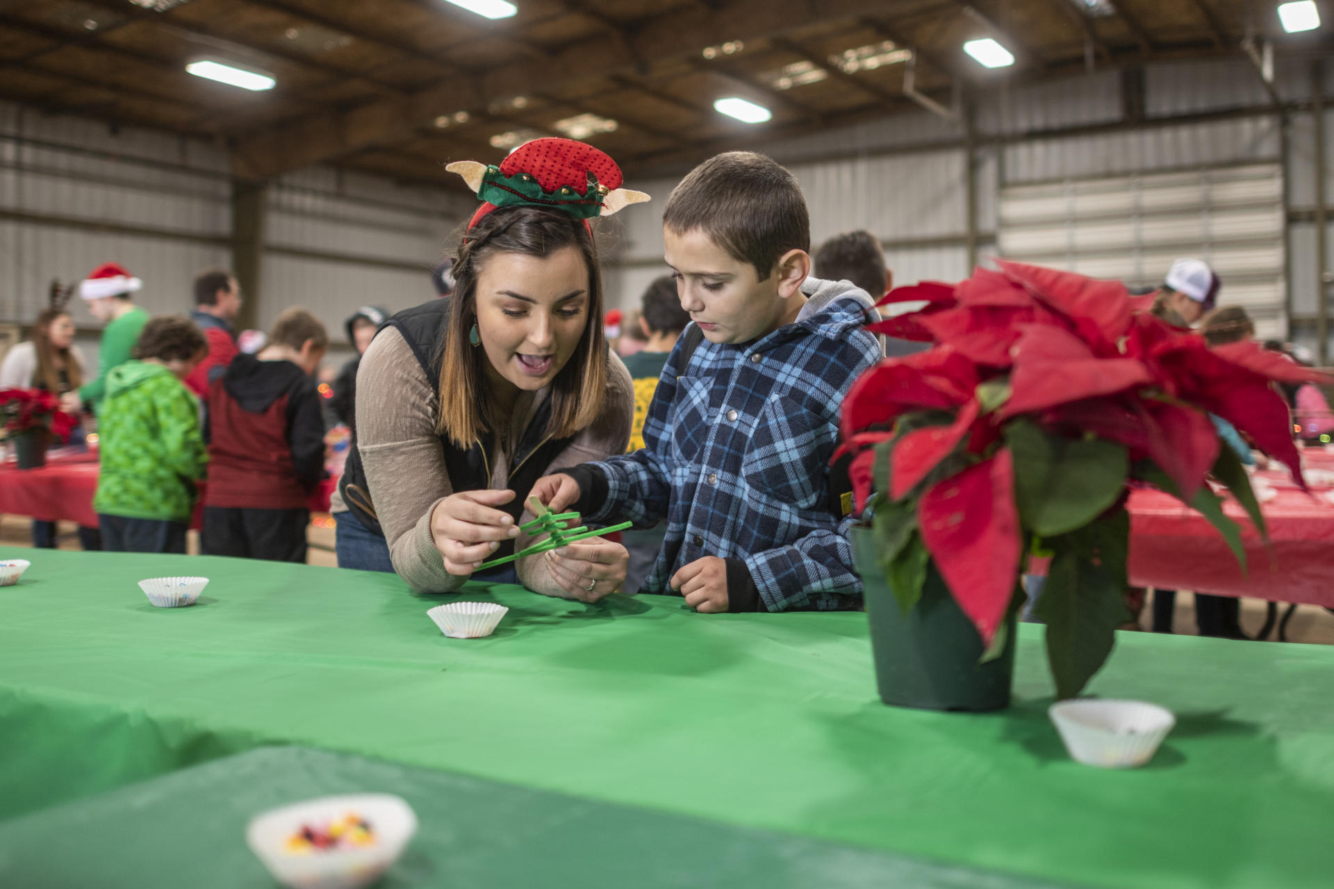 A student helps a young boy make a Christmas tree out of green pipecleaners.
