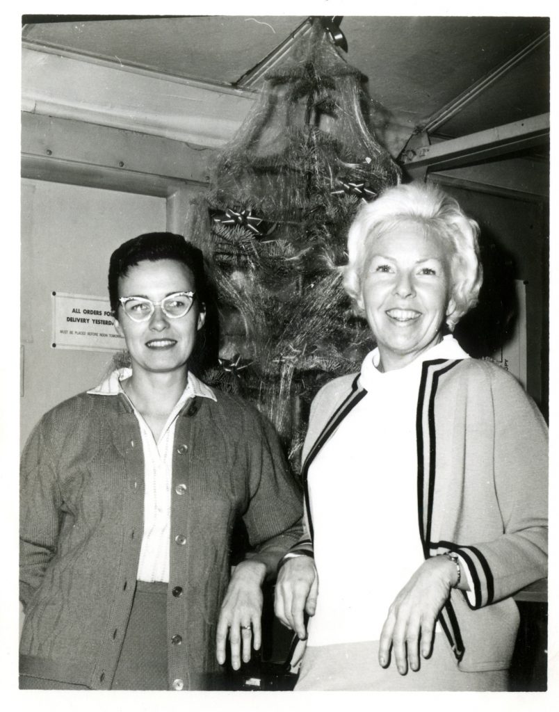 Black and white photo of Faye and another woman standing in front of a Christmas tree.