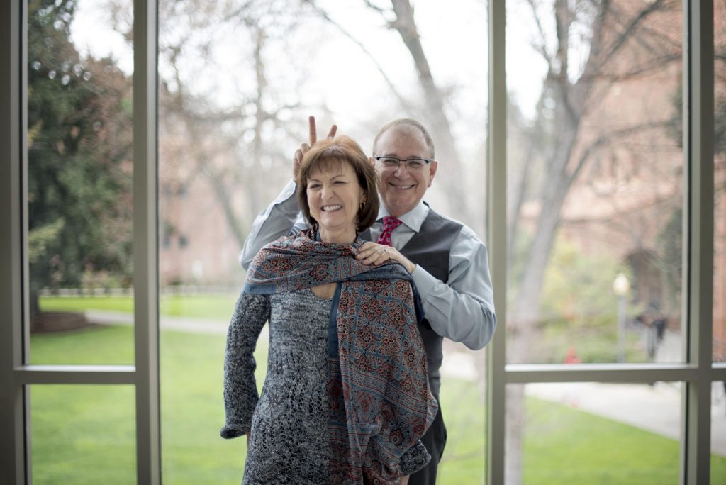 Eddie Vela holds up "bunny ears" behind Celeste Jones while standing in front of Arts Building windows that overlook campus.