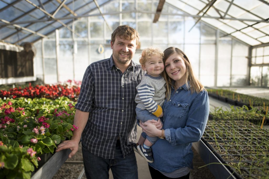 Matt, Ollis, and Lauren Housley stand between rows of flowers and plants in the greenhouse.
