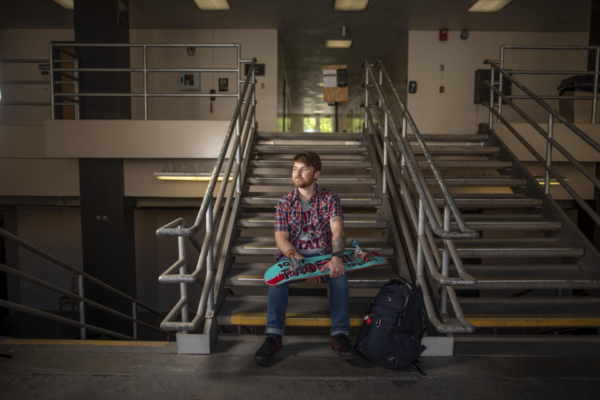 Anthony McKinney sits on a short flight of stairs holding his skateboard.
