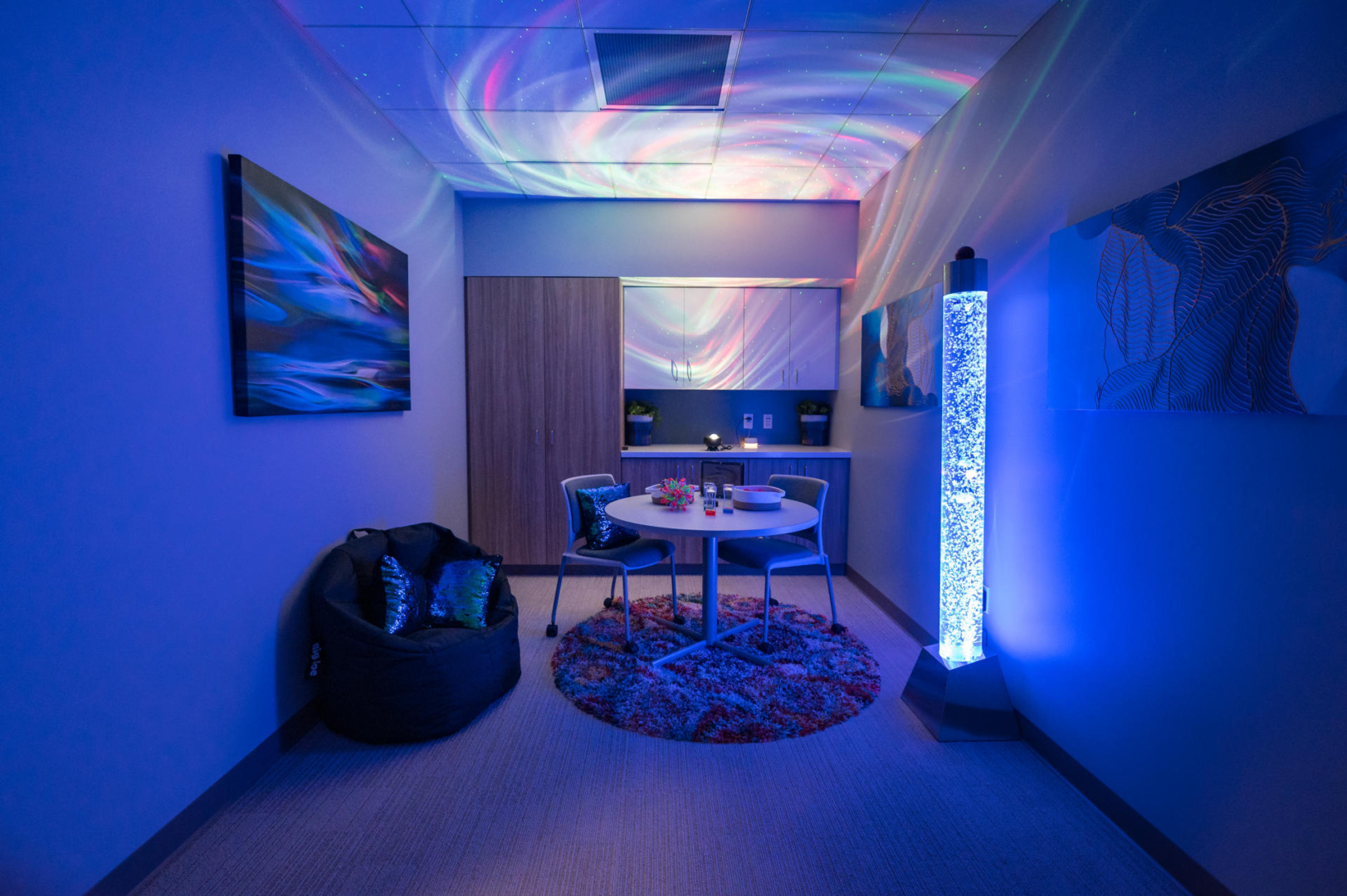 A sensory room with soft blue lights, a table and a beanbag chair 