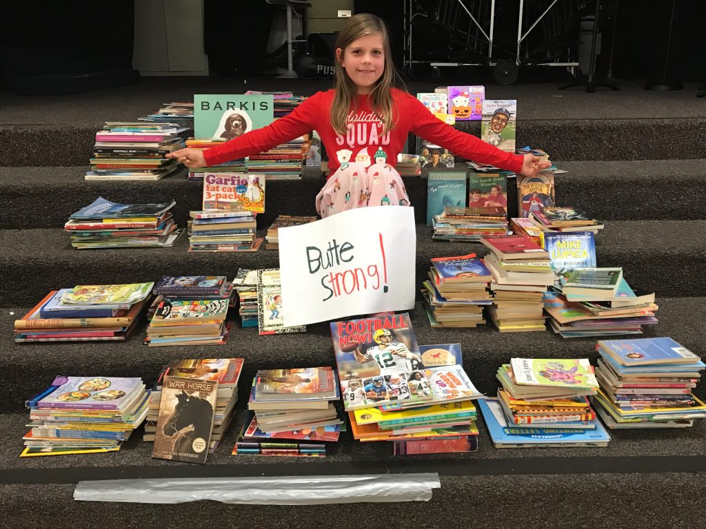 Isla Aguilar sits among piles of books with a sign that reads "Butte Strong!"