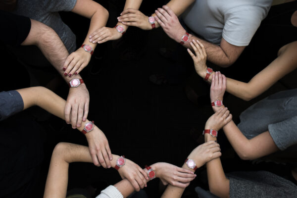 To convey a team effort, students lock arms in a circle to showcase their red watches, which signal they can intervene in risky situations related to drugs and alcohol.