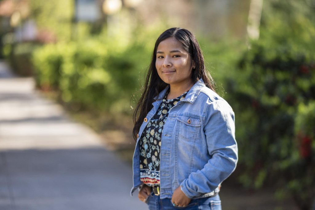 Cecilia Apolinar dressed in a denim jacket poses for a portrait on campus.