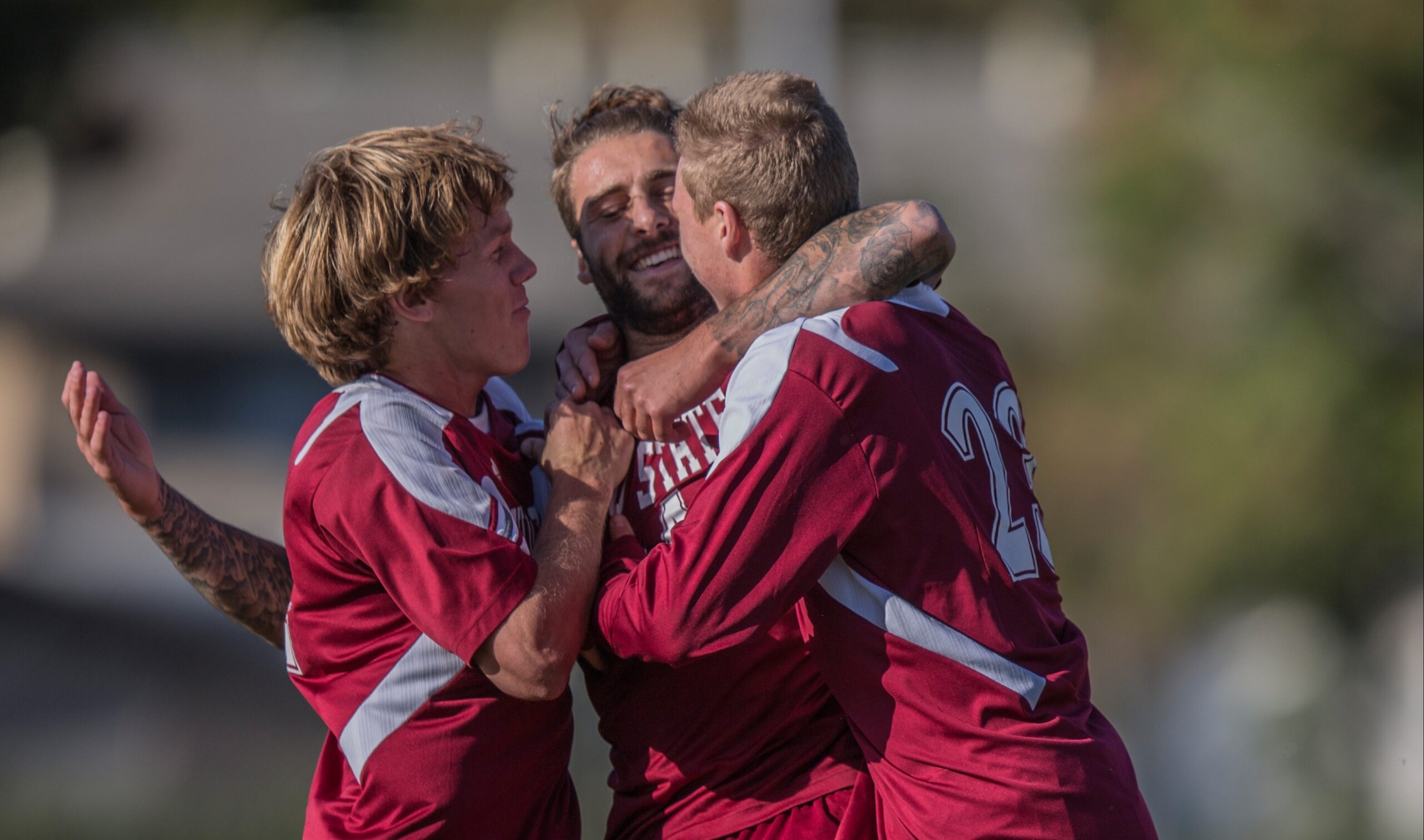 Three men's soccer players embrace in celebration after a game-winning goal.