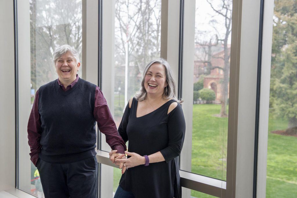 Sandra Beck and Sara Cooper laugh and hold hands in the Arts and Humanities Building.