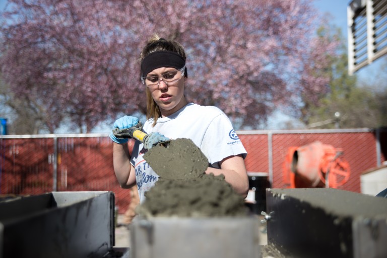 Student in safety glasses shovels concrete into a mold