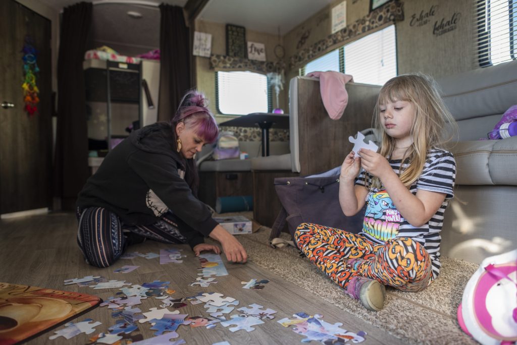 Sabrina Hanes and her 5-year-old daughter, Aroara, work together to assemble a children's puzzle on the floor of the trailer they are living in after the Camp Fire.
