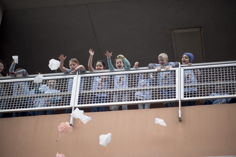 Children throw parachute toys off a ledge for Imagineer Day.