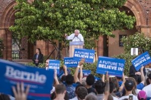 Bernie Sanders at a podium in front of a crowd waving signs.