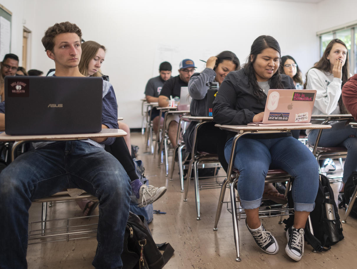 Valerie Olivares sits with her laptop open in the front row of a classroom filled with students at their desks.