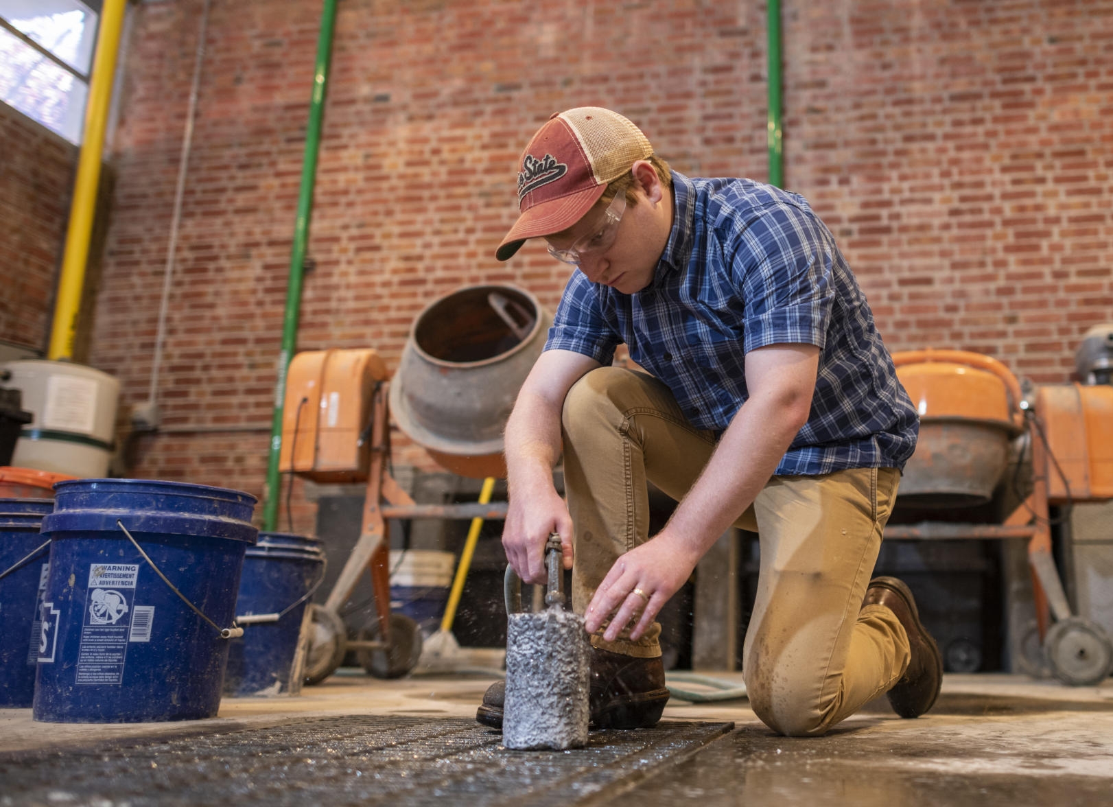 Tim O'Shea sprays water on a cylinder of concrete over a metal grate in the concrete lab.
