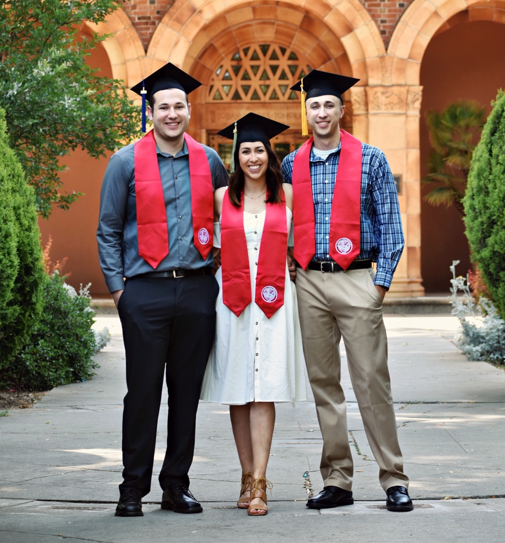 Siblings Nick, Kayla, and AJ Gonzales wear their Chico State stoles as they stand in front of Kendall Hall's "Today Transforms Tomorrow" lettering.