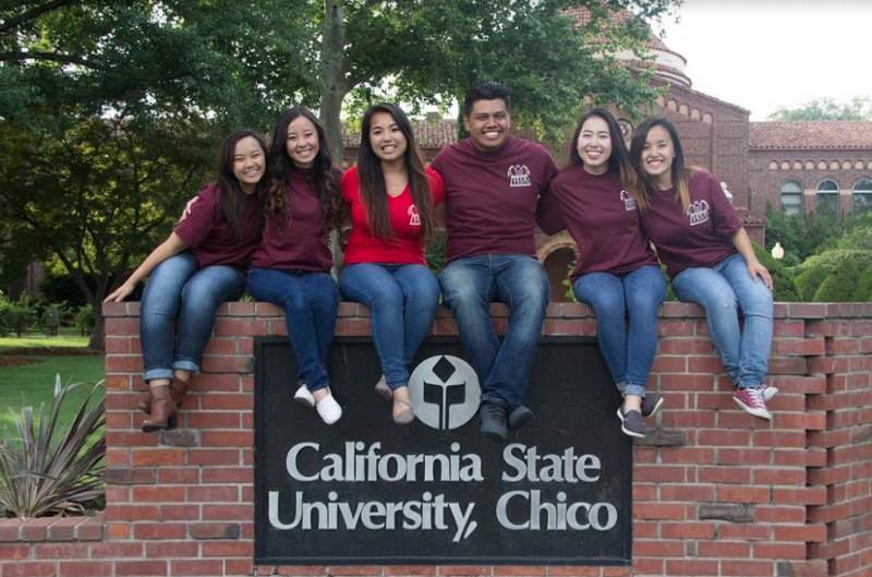A group of students sits on top of the California State University, Chico sign.
