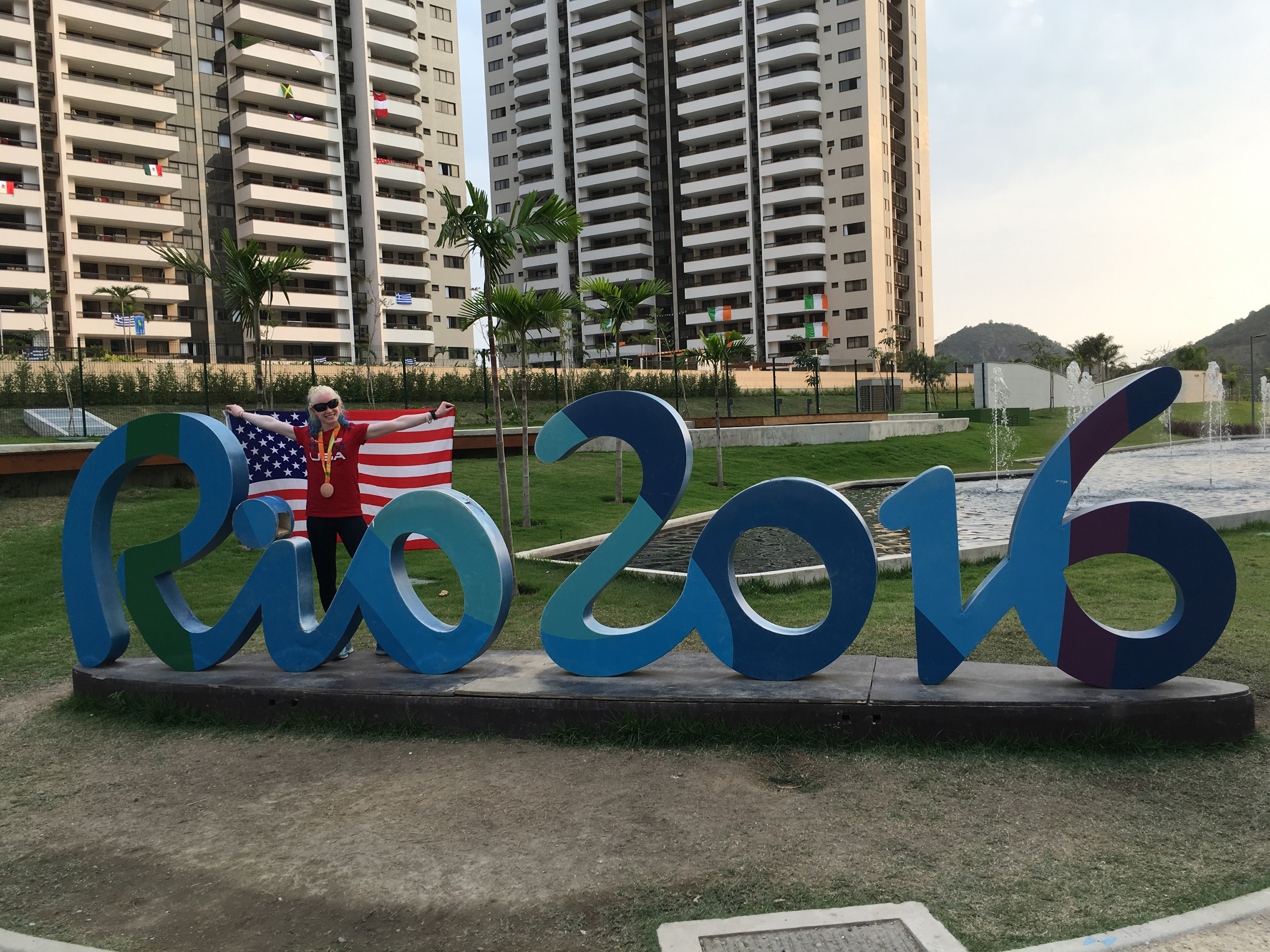 Kym Crosby waves the American Flag and stands behind the Rio 2016 Paralympic sign.