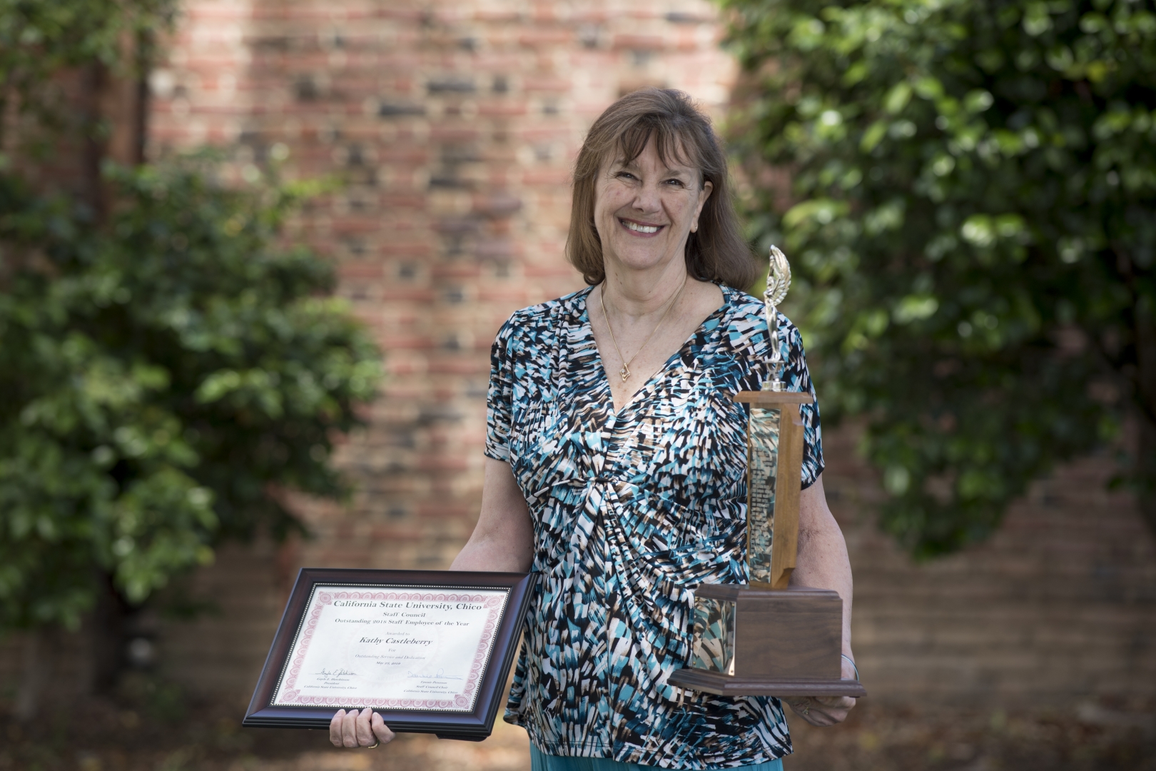 Kathy Castleberry smiles and holds a plaque and trophy, earned for winning Outstanding Staff Employee of the Year.