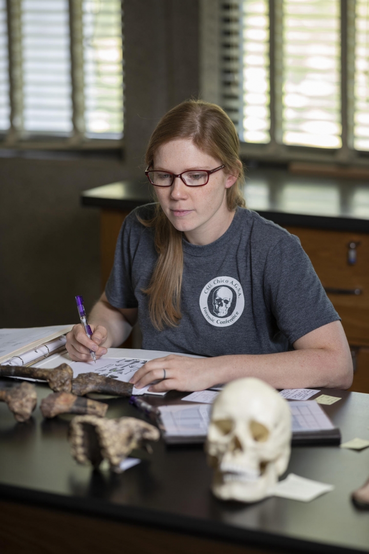 Jaqueline Galimany takes notes on a diagram of the human skeleton while looking at bone fragments on a table.