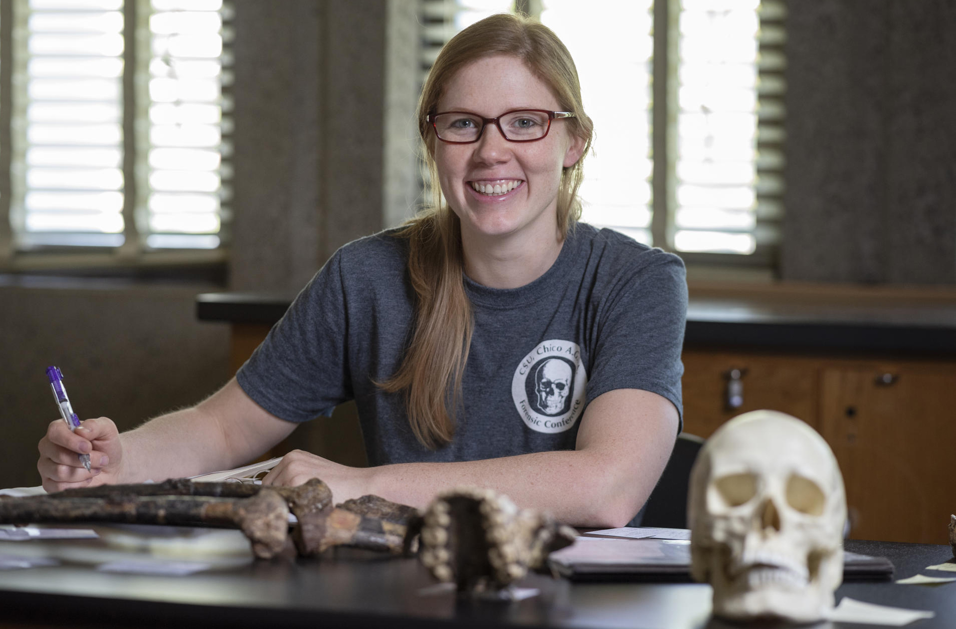 Jacqueline Galimany sits at a table with bone artifacts and a skull, prepared to take notes.