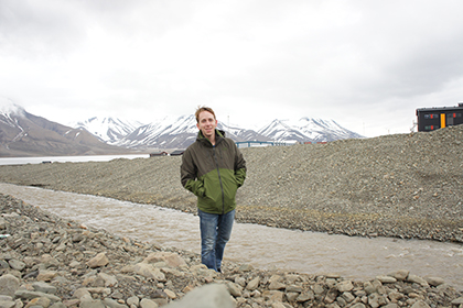 Matthew Stone standing beside a rocky stream with snow-capped mountains in the background,