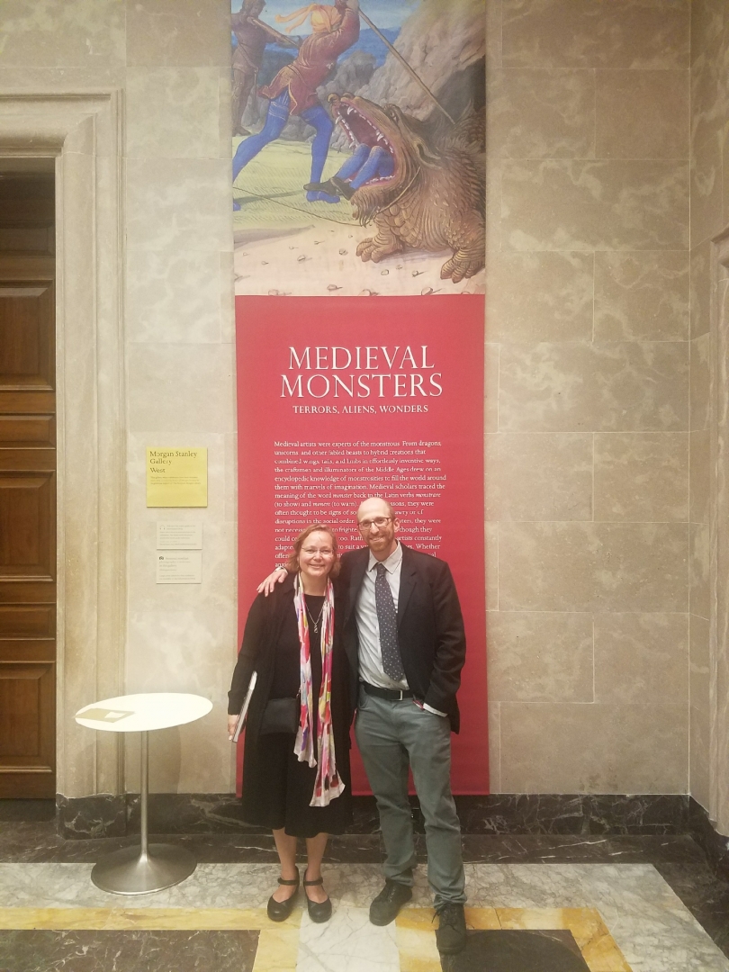Sherry Lindquist and Asa Mittman pose in front of a promotional banner for their exhibit at The Morgan.