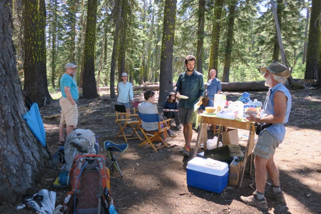 A group of hikers gather around refreshments and talk.