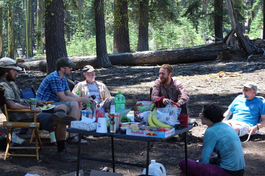A group of hikers sit around a table of refreshments.